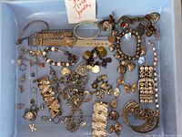 Overview of mixed silver toned jewelry pieces including bracelets, charms, cuff bracelets, a wristwatch, and a rhinestone bracelet arranged in a box.
