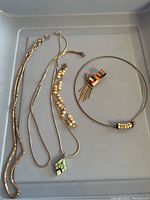 Photo shows the lot of five jewelry items laid out on a grey tray including multiple silver chains, a pearl necklace, a choker with a silver bead, and a pendant.