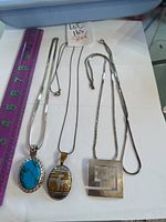 Three sterling silver necklaces displayed with a ruler for size reference, showing a variety of pendant styles and a chain.