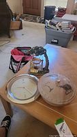 Photo of all three items on a wooden table: wall clock, stone elephant bowl with lid, and painted wood candle swing