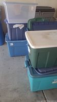 Photo showing multiple plastic storage totes in various colors and sizes, mostly stacked with lids, some without lids.