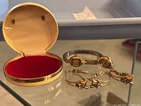 Photo showing two vintage women's watches and a vintage watch band with gem accents next to an open round display case with red velvet interior.