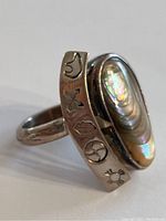 Close up clear photo of the ring showcasing the iridescent gemstone and symbolic engravings on the band.
