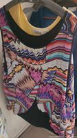 Multicolor geometric patterned women's top on hanger with black collar and long sleeves.