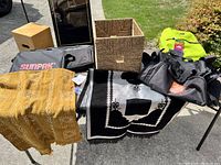 Shows all items including rugs, bags, wicker basket, and box arranged on table outdoors