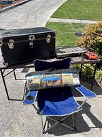 Side view showing the camping chair with the canopy package on it, the storage trunk, and the table with tools.