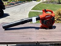 Side profile of orange Echo gas leaf blower with black blower tube on table outdoors.