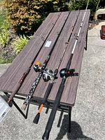 Three fishing poles on table, all fitted with reels, showing full length of rods and grips