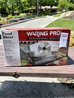 Box of Waring Pro professional food slicer on table outdoors, showing front branding and product image.