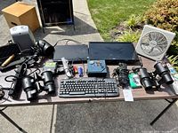 Wide view showing various electronic and household items spread on a table including keyboard, fans, lights, power strip and smaller items.
