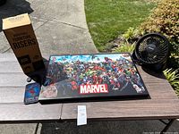 Photo shows assembled Marvel puzzle in a frame, box of adjustable furniture risers, small portable fan, and a Game of Thrones phone case.