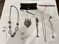 Full view of all jewelry items laid out on white paper, showing necklaces, rings, bracelets, brooch, and hairpin