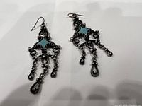 Close-up of silver-tone dangle earrings with intricate metalwork and turquoise triangle accents.