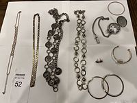 Jewelry lot arranged on white paper on flat surface, showing all items in the lot including necklaces, bracelets, earrings, and watch.
