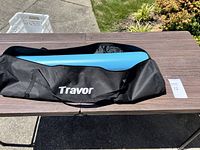 Black Travor branded carrying bag with blue padding inside placed on a wooden table outdoors.