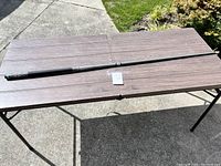Full length view of the two-piece pool stick laid out on a wooden table outdoors, showing its black finish and design details.