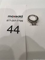 Top-down view of the silver-tone ring placed next to a MaxSold number card for scale and identification.