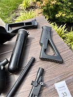 Close up of black shoulder stock, CO2 cartridge, and tank components photographed outdoors.
