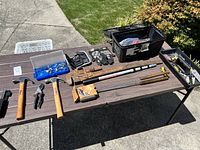 Wide view of toolbox assortment on table outside including large wrench, hammers, gloves, socket set and toolboxes.