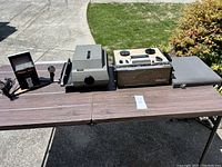 Full view of the three electronics items on a brown table outdoors with greenery and driveway in the background.