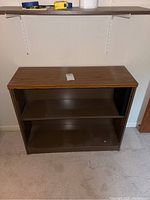 Front view of wooden top and dark brown metal bookcase with two shelves.