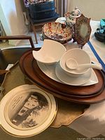 Photo showing white porcelain bowls, Asian ceramic bowl, ginger jar, decorative plates, and trays arranged on table.