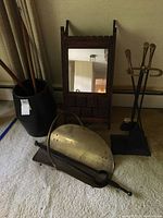 Wood wall cabinet with mirror, ceramic pot log holder with wooden tools, metal fireplace tool set with stand, brass firewood holder, and curved black metal tool arranged on floor