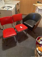 Two red vinyl retro chairs and one black leatherette barrel chair positioned closely together showing upholstery and frame details.