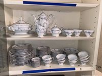 Wide view of china set on shelves showing many plates, cups, and serving pieces in white porcelain with blue floral motifs and silver trim.