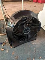 Black Lasko fan with circular front grille and visible blades, showing wear.