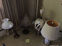 Four lamps arranged on carpet near curtain backdrop showing variety of bases and shades.