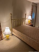 Photo showing both yellow glass base lamps with white lamp shades on either side of a brass bed frame in a bedroom setting.