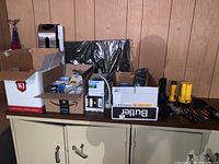 Wide view of lot items including boxes of lightbulbs, flashlights, gloves, and tools on cabinet.