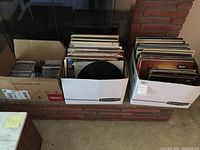 Photo showing three containers: two with vinyl records and one with CDs, all in cardboard boxes with album covers showing.