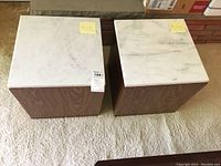 Two square side tables with white marble tops and dark laminate wood grain bases sitting on carpet.