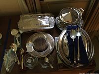 Full view of silver plated serving pieces including covered casseroles, trays, footed bowl, cheese server, condiment bowls, and serving utensils