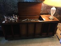 Large wooden stereo cabinet closed, showing paneled front and some silver trophies on top.