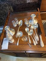 Overview of two weighted sterling candlesticks, four glass salt and pepper shakers with sterling tops, assorted sterling serving utensils and spoons on wood surface