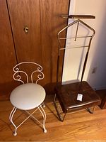 Both stools side by side showing white metal vanity stool with round cushioned seat and brown leather valet stool with wooden tray and hanger.