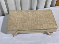 Front angled view of rectangular vintage jewelry box with cream vinyl-patterned padded lid and pale pink plastic base with angular supports.