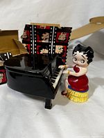 Side view of Betty Boop porcelain figurine seated at black grand piano music box with original box behind