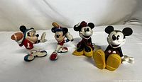 Four Disney Enesco figurines: two sporting Mickey Mouse, seated Minnie and Mickey Mouse figures. White background studio photo.