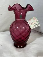 Front view of cranberry glass vase with original tag and Fenton sticker visible.