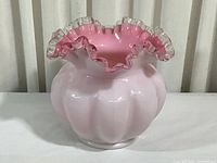 Front view of a white opalescent glass vase with a pink interior lining and a clear ruffled edge.