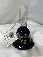 Full view of the purple glass bell with handpainted flowers and clear twisted handle showing tag attached.