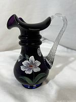 Full view of Fenton purple glass mini pitcher vase, showing flared ruffled rim, twisted clear glass handle and painted florals