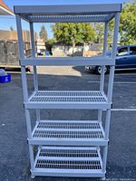 Front view of assembled white 5-shelf plastic shelving unit with black rails, showing slatted shelf design and stable base.