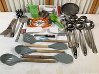 Overview of assorted kitchen utensils including ladles, measuring cups, and spoons laid on a white surface.