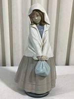 Front full view of Lladro NAO peasant girl figurine showing detailed shawl and blue bag.