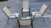 Four matching outdoor patio chairs arranged in a parking lot, showing overall condition and style.